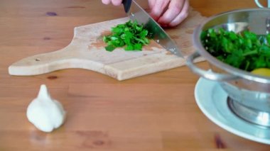 Tahta kesme tahtasına maydanoz kesen bıçaklı bir kadın eli.