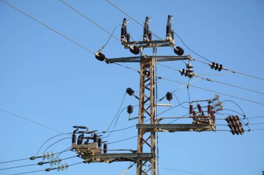 Mavi gökyüzünün altındaki elektrik dağıtım direğinin ve elektrik hatlarının üst kısmının düşük açılı yakın çekim görüntüsü