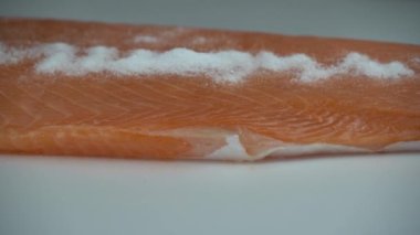 Kauçuk eldivenli biri çiğ somon filetosuna nazikçe tuz sürüyor. Tuzlanmış somon hazırlama
