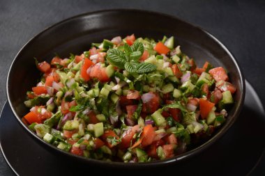 Domatesli Shirazi Salatası, salatalık, kırmızı soğan, maydanoz ve siyah kasede taze limon suyu. Persian Shirazi sebze salatası yakın plan. Popüler İsrail yemekleri