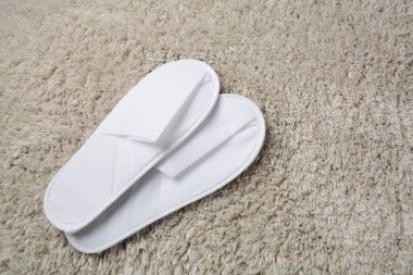 White slippers on grey mat. Pair of comfortable slippers in hotel room