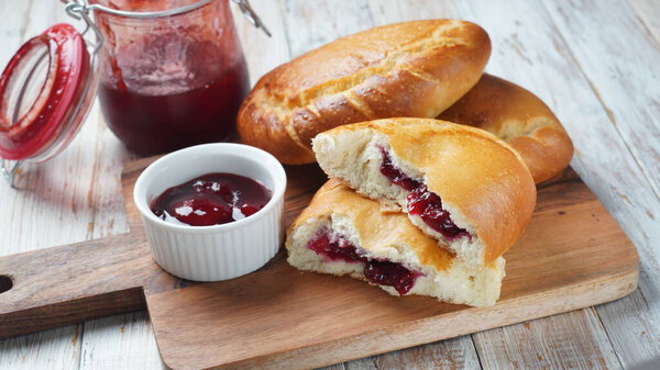 Вишневые пироги с ягодами вишни, миска с вишневым джемом. Домашние сладкие пироги из дрожжевого теста, свежеиспеченного в духовке