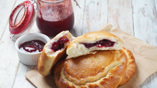 Вишневые пироги с ягодами вишни, миска с вишневым джемом. Домашние сладкие пироги из дрожжевого теста, свежеиспеченного в духовке