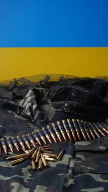 Mavi-sarı Ukrayna bayrağı, 5.56 mm mühimmat, makineli tüfek mermisi kemeri, şarjörlerde tüfek mühimmatı, Ukrayna üniforması ve ordu siyah şapkası.