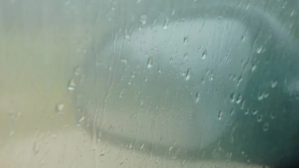 Arka planda ayna olan bulanık yağmur damlaları arabanın camına düşer. Kapat.