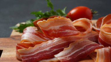 Tütsülenmiş domuz pastırması, otlar ve kiraz domatesleri, dilimlenmiş domuz pastırması, tahta kesme tahtası.
