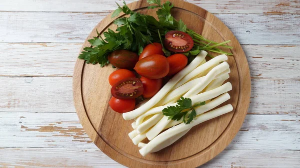 String cheese or cheese whip - salty snack cheese with cherry tomatoes and herbs on chopping board. Turkish cheese