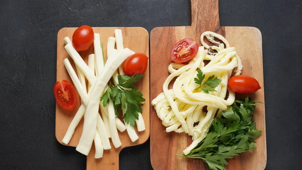 String cheese or cheese whip - salty snack cheese with cherry tomatoes and herbs on chopping board. Turkish cheese
