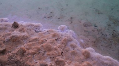 Ölü denizin kıyısında birikmiş büyük tuz birikintisi. Maden tuzu yatakları, Ölü Deniz 'in tipik manzarası. Güneş doğarken kumsalda tuz.