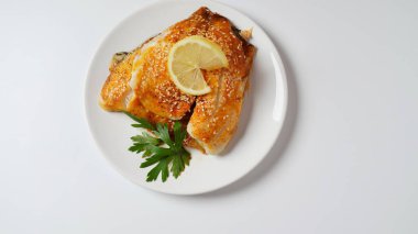 Fresh backed tilapia fillet on white plate with lemon and herbs