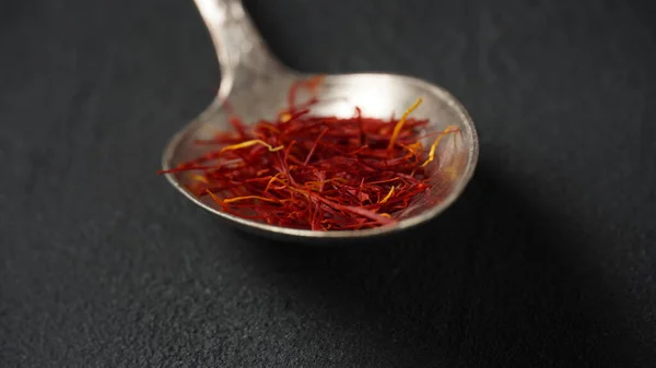 Expensive Red Dried saffron spice in a spoon on dark background