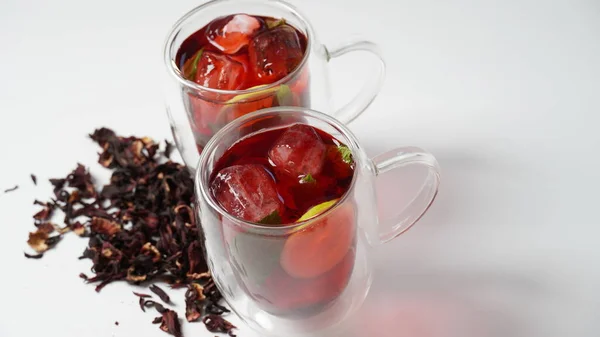 Hibiscus cold tea drink with ice cubes and lemon in glass