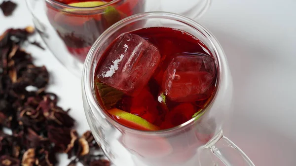 Hibiscus cold tea drink with ice cubes and lemon in glass