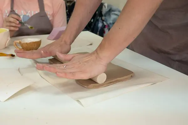 Γυναικείος κεραμίστας ρολά πηλό χρησιμοποιώντας ξύλινη πλάστη σε κεραμικό στούντιο. Κοντινά χέρια. Δημιουργία κεραμικής — Φωτογραφία Αρχείου