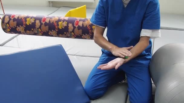 Fysiotherapeut toont massage oefening voor gevoeligheidsherstel met geribbelde bal in sensorische integratieruimte. — Stockvideo