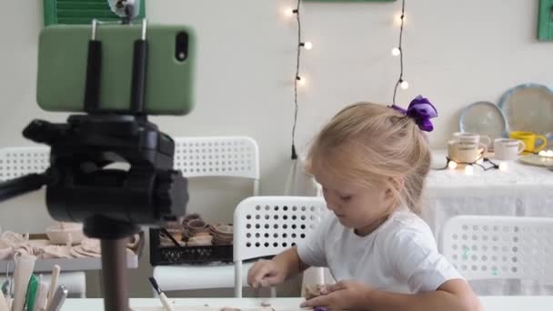 Chica vlogger grabación de vídeo con arcilla de modelado y hablando para la cámara del teléfono inteligente. Blogger infantil en un estudio de cerámica creando contenido interesante para niños — Vídeos de Stock