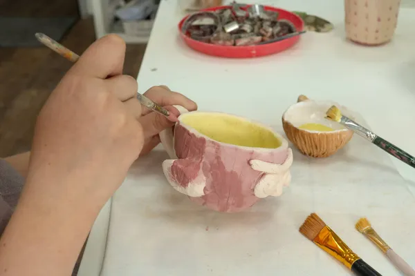 Child girl painting with brush on clay pottery cup in ceramic workshop studio. Development of art and painting in children — Stock Photo, Image