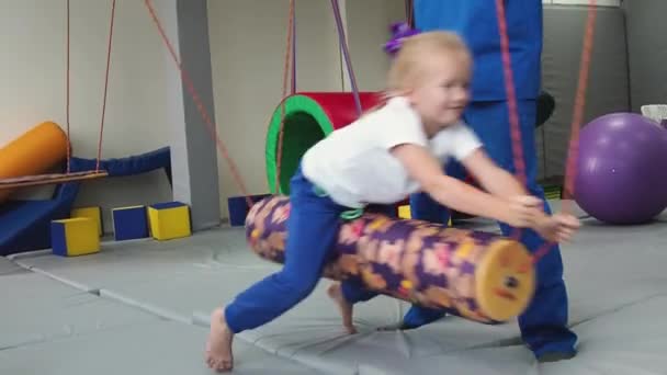Kind meisje met fysiotherapeut swingen op swing tijdens zintuiglijke integratie sessie. Ontwikkelingsfuncties van het vestibulair apparaat bij kinderen. — Stockvideo