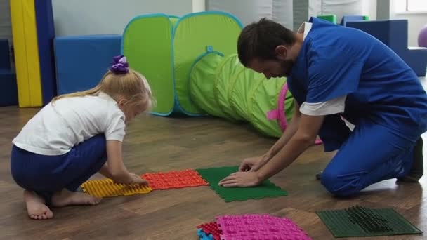 Niño con terapeuta ensambla alfombra de masaje para la lección de integración sensorial. Masaje de pies para prevenir pies planos en niños y aliviar la tensión. — Vídeo de stock