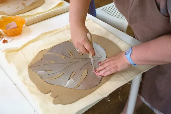 Vrouw hand pottenbakker maken klei monstera blad in aardewerk atelier. Proces van het maken van keramische vaas. Handgemaakt, hobby kunst en handwerk concept — Stockfoto