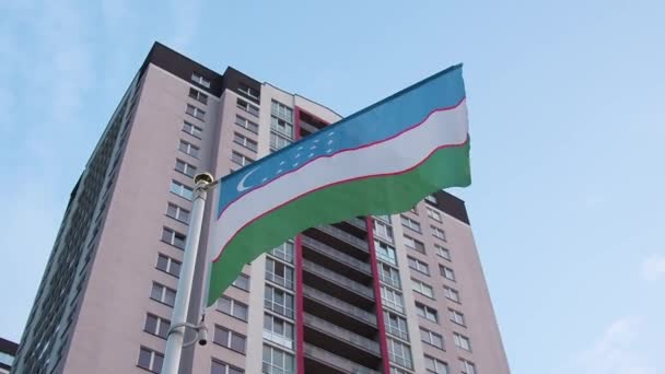 Uzbekistan flag waving in slow motion against clean blue sky and house — Stock Video