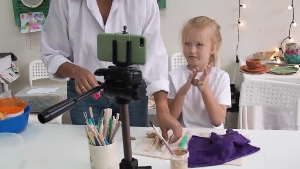 Flicka vlogger inspelning video med modellera lera och talar för smartphone kamera. Unge bloggare i en keramisk studio skapa intressant innehåll för barn — Stockvideo