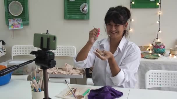 Mujer tutora de cerámica en el estudio de arte grabar vídeo lección para el curso de cerámica en línea o dirige una clase magistral de vídeo sobre la creación de productos de cerámica. vlogger grabación de vídeo con modelado de arcilla. — Vídeos de Stock