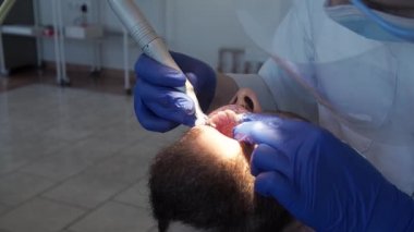 Profesyonel dişçi kadın diş hekimi, diş sağlığı kliniğindeki bir hastanın dişlerine özel bir macun sürer. Ağız boşluğuna hijyen bakımı. Stomatoloji kliniğinde diş temizliği.