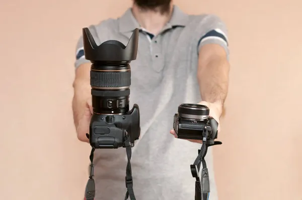 Muž drží v jedné ruce dslr fotoaparát a v druhé bez zrcadla. Porovnání dvou kamer pro natáčení. Výběr před nákupem a vyhodnocením klady a zápory kamer. — Stock fotografie