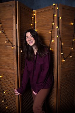 Güzel romantik esmer kadın rahat çatı katında pijamalı, çelenkli ve ahşap perdeli. Otantik kadın portresi.