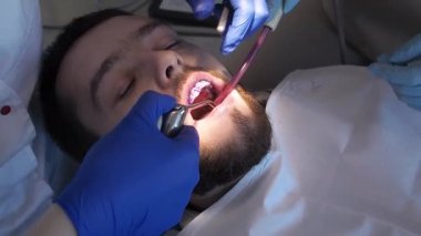 Diş hekimi, erkeğin dişlerini yakından gören mavi jöleyi yıkar. Hastaların ağız boşluğu için hijyen bakımı. Diş hekimliğinde ya da stomatoloji kliniğinde diş temizliği