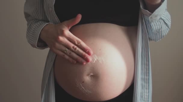 Hamile bir kadın göbeğine gerilme izi temizleme losyonu sürüyor. Doğumdan sonra cilt bakımı ve çatlakların önlenmesi. — Stok video