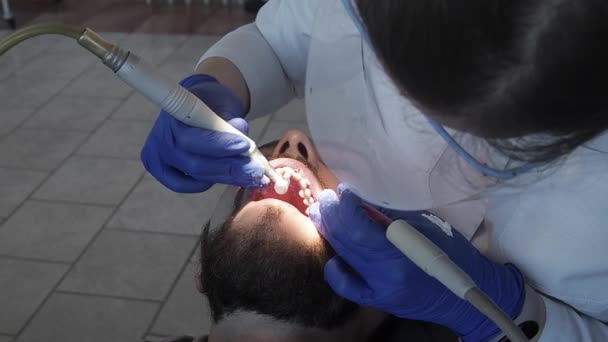 Femme médecin dentiste professionnel applique une pâte spéciale sur les dents d'une patiente dans une clinique dentaire. Soins d'hygiène pour la cavité buccale. Nettoyage prophylactique des dents dans une clinique de stomatologie. — Video