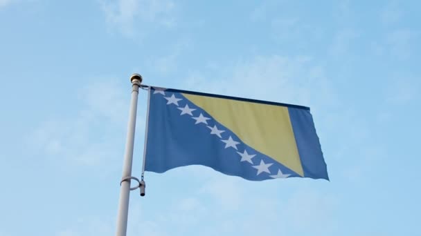 ボスニア・ヘルツェゴビナ風になびく旗竿で旗を掲げ、雲を背景に空を舞う. — ストック動画