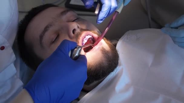 Tandarts is wast af blauwe gel van mannen tanden closeup view. Hygiëne zorg voor patiënten mondholte. profylactische reiniging van tanden in de tandheelkunde of stomatologie kliniek — Stockvideo