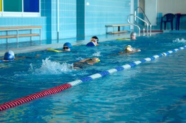 Havuzda yüzme eğitimi. Gençler ve erkekler serbest stil yüzmeyi öğrenirler.