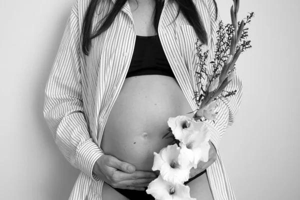 Tampilan samping otentik wanita hamil santai dengan bunga di kemeja dengan perut telanjang besar. kehamilan sehat. — Stok Foto