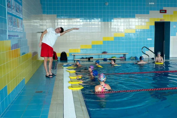 Minszk, BELARUS - 2021. október 30: Csoportos lecke egy edzővel a medencében. Az edző kiosztja és ellenőrzi a teljesítési technikát.. — Stock Fotó