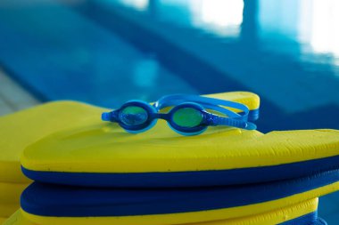 Spor merkezinde yüzme havuzunun yanında renkli yüzme tahtaları yığını var.