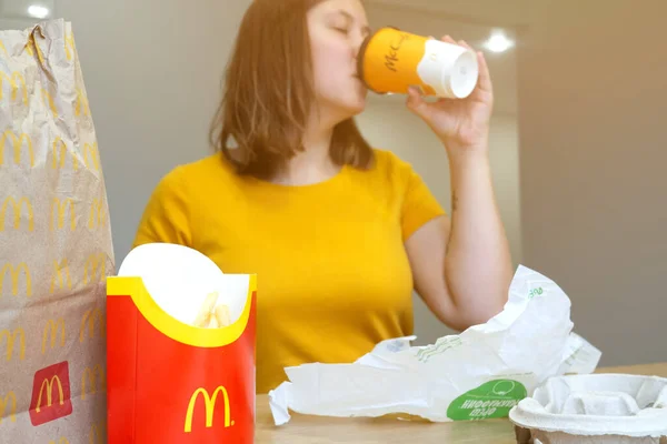 Dostawa McDonalda w papierowych torbach podczas kwarantanny. Młoda kobieta je pyszne jedzenie na wynos w domu. Mińsk, BELARUS - 1 października 2021 r. — Zdjęcie stockowe