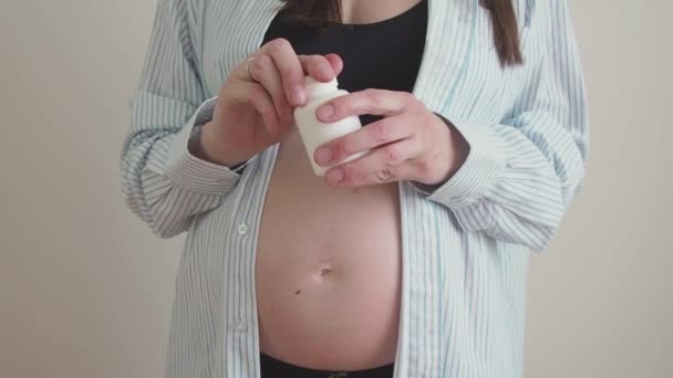 Donna incinta irriconoscibile mette pillole in mano da un barattolo vicino alla pancia. Uso di integratori alimentari o vitamine durante la gravidanza — Video Stock