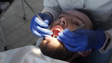Kadın dişçi, dişçi aletinin yardımıyla hastanın ağız boşluğunu yakından inceliyor. Koruyucu diş hijyeni ve kontrol
