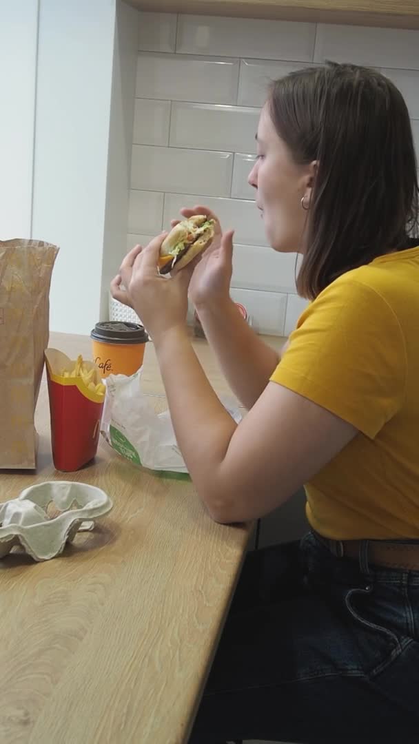 若い女性が自宅でおいしい高速テイクアウト食品ハンバーガーを食べています 隔離中の食品配送の概念 孤独と孤独の過剰摂取とストレス Minsk Belarus 2021年10月1日 — ストック動画
