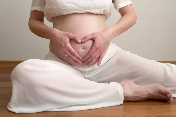 Donna incinta seduta sul pavimento in posa kapotasana e fare a forma di cuore mano mostrare amore. concetto di gravidanza sanitaria. — Foto Stock