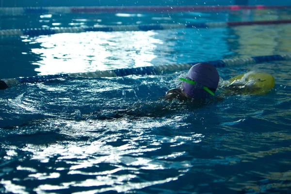 Невизначений дитина плаває вільний стиль тренування в плавальному басейні з бризкою води . — стокове фото