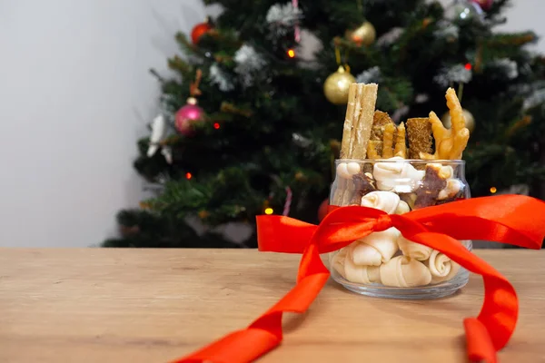 Stillleben von Hundefutter und gesunden Leckereien mit roter Schleife auf Christbaumhintergrund mit Kopierfläche. Weihnachtsgeschenk für Haustiere. — Stockfoto