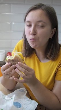 Genç bir kadın, evde lezzetli fast-away yemek hamburgeri yiyor. Karantina sırasında yemek teslimatı konsepti. Yalnızlık ve yalnızlıkta aşırı yemek ve stres.