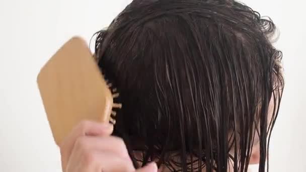 Woman brushing with combs tangled hair with conditioner after shower slow motion. — Stock Video