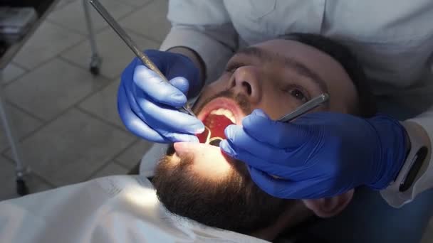 Kadın dişçi, dişçi aletinin yardımıyla hastanın ağız boşluğunu yakından inceliyor. Koruyucu diş hijyeni ve kontrol. — Stok video