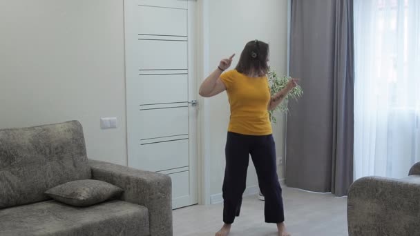 体の正の概念。幸せな柔軟な太りすぎの女性面白いダンスのスローモーションと家でヘッドフォンで音楽を聴く. — ストック動画
